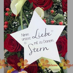 Könnte beinhalten: Eine weiße sternförmige Karte mit dem Text "Nimm unsere Liebe mit zu deinem Stern" (Nimm unsere Liebe mit zu deinem Stern) umgeben von roten Rosen und weißen Blumen.