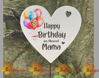 Może przedstawiać: Biały palik ogrodowy w kształcie serca z czarnym napisem "Happy Birthday im Himmel Mama". Palik posiada akwarelową ilustrację kolorowych balonów i małe wycięcie w kształcie serca.