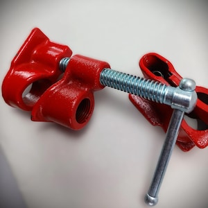 Puede incluir: Dos abrazaderas de tubería de metal rojo con un tornillo roscado plateado y un mango plateado. Las abrazaderas se utilizan para sujetar las tuberías juntas.