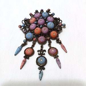 May include: Vintage floral brooch with a dark metal filigree design. The brooch features clusters of pastel-colored, shell-shaped elements with rhinestone centers. Dangling accents in coordinating colors complete the design. A unique piece of vintage jewelry.