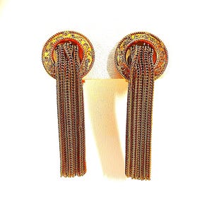 May include: A pair of gold-toned earrings with a circular design and intricate detailing. The earrings feature long, dangling chains that cascade downwards. The design is ornate and elegant, suitable for formal occasions.