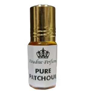 May include: A small, clear glass bottle with a gold cap. The bottle contains a yellow liquid and has a white label with black text that reads "Paradise Perfume Pure Patchouli".