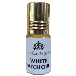 Op de afbeelding: Een klein, doorzichtig glazen flesje met een gouden dop en een wit etiket. Het etiket heeft een kroonontwerp en de tekst "Paradise Perfumes WHITE PATCHOULI".
