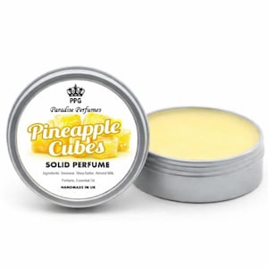 Op de afbeelding: Zilveren blikje met vaste parfum met de tekst "Pineapple Cubes" in geel. Het etiket bevat ook de tekst "Paradise Perfumes" en "HANDMADE IN UK". De parfum heeft een lichtgele kleur.