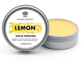 Może przedstawiać: Srebrny pojemnik z żółtą etykietą, na której widnieje napis "PPG Paradise Perfumes LEMON SOLID PERFUME" z logo korony. Etykieta zawiera również listę składników: wosk pszczeli, masło shea, olej migdałowy, perfumy, paczula, olejki eteryczne ylang ylang. Pojemnik jest wykonany ręcznie w Wielkiej Brytanii.