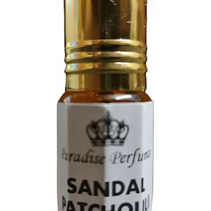 Puede incluir: Pequeña botella de vidrio transparente con tapa dorada. Contiene un líquido marrón claro y una etiqueta blanca con "Paradise Perfumes" y "Sandal Patchouli". Un diseño de corona está encima del texto.