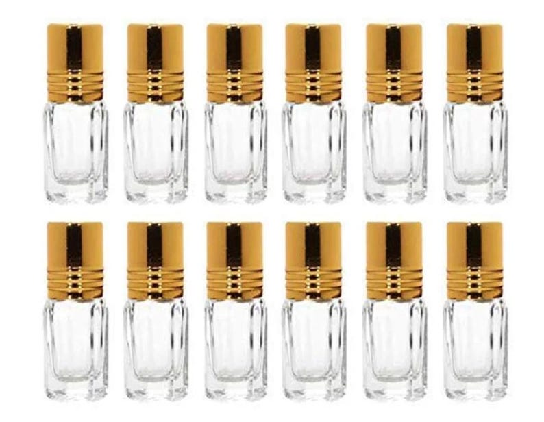 May include: Ten clear glass bottles with gold lids. The bottles are rectangular and have a slightly textured surface. The lids have a gold band around the top.