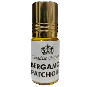 Peut inclure: Un petit flacon en verre transparent avec un bouchon doré. Le flacon contient un liquide jaune et porte une étiquette blanche avec du texte noir qui indique "Paradise Perfume Bergamot Patchouli".