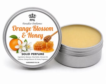 Może przedstawiać: Srebrna puszka z perfumami w sztyfcie z napisem "Orange Blossom & Honey". Etykieta przedstawia pomarańczę, białe kwiaty i plaster miodu z kapiącym miodem. Otwarta puszka ukazuje jasnożółty balsam. "Handmade in UK."