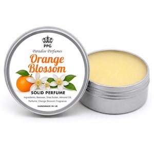 Puede incluir: Una lata plateada de perfume sólido "Orange Blossom" de Paradise Perfumes. La etiqueta presenta una naranja, flores blancas y hojas verdes. La lata abierta revela un perfume sólido de color amarillo claro. Hecho en el Reino Unido.