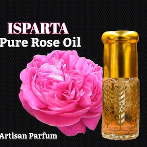 May include: A small bottle of Isparta Pure Rose Oil with a gold cap. The bottle is clear and shows a light pink liquid inside. A pink rose is in the background.