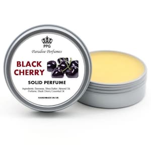 Op de afbeelding: Een zilveren blik met een vaste parfum met zwarte kers. Het etiket vermeldt "PPG Paradise Perfumes Black Cherry Solid Perfume" en somt de ingrediënten op: Bijenwas, Shea Butter, Amandel Olie, Parfum, Zwarte Kersen Essentiële Olie. Het etiket vermeldt ook "Handgemaakt in het Verenigd Koninkrijk".