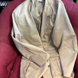 May include: A beige utility jacket with a button closure and two large pockets on the front. The jacket is made of a lightweight fabric and has a relaxed fit.