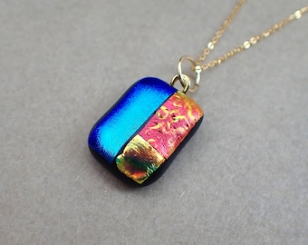 May include: A blue and red glass pendant with gold accents hangs from a gold chain. The pendant is rectangular and has a layered design.