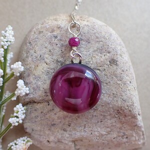 May include: A silver chain necklace with a round, purple glass pendant and a small, purple bead accent.