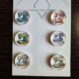 May include: Six handmade glass magnets with watercolor illustrations of vintage sewing machines in various colors, including blue, pink, green, and purple. The magnets are arranged on a white card with the text "Cabochon Design Studio" and "Handmade Glass Magnets".