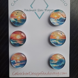 May include: Six round glass magnets with a sunset over the ocean scene. The magnets are on a white background with the text "Cabochon Design Studio" and "Handmade Glass Magnets".
