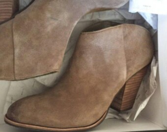 May include: A pair of tan suede ankle boots with a stacked wooden heel. The boots are in a box with tissue paper. The boots have a rounded toe and a side zipper. The heel is approximately 3 inches high.