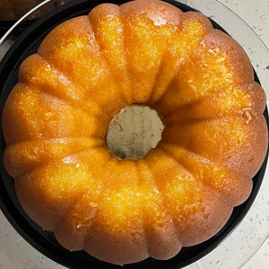 May include: A golden yellow bundt cake with a shiny glaze, sitting on a black and white cake stand.