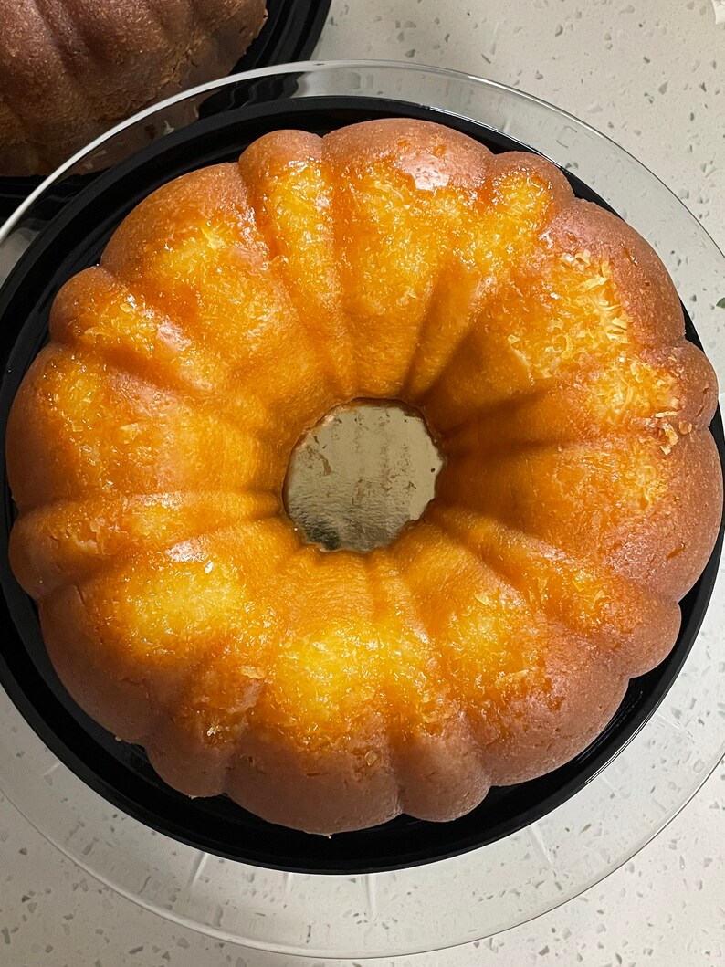May include: A golden yellow bundt cake with a shiny glaze, sitting on a black and white cake stand.