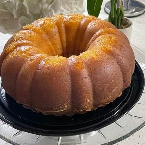 May include: A golden yellow bundt cake with a glazed finish, sitting on a black cake stand and a clear glass pedestal.