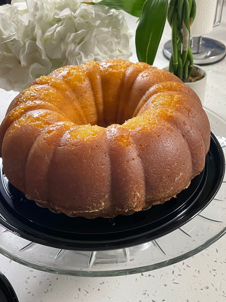 May include: A golden yellow bundt cake with a glazed finish, sitting on a black cake stand and a clear glass pedestal.