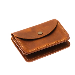 May include: A small, brown leather wallet with a snap closure. The wallet is rectangular with rounded corners and visible stitching. The leather has a slightly distressed appearance.