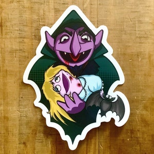 May include: A purple monster with fangs and a green cape holds a pink puppet with blonde hair. The monster has a red mouth and a red stain on its chin. The puppet has a blue dress and a white pearl necklace. A small brown bat with white eyes is flying behind the monster.
