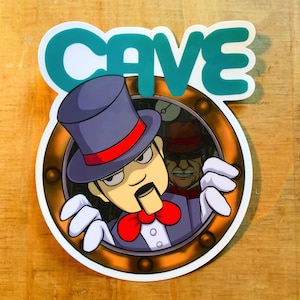 Può includere: Un'illustrazione di un uomo dei cartoni animati che indossa un cappello a cilindro e un papillon, che sporge da un oblò rotondo. L'oblò è circondato da una cornice dorata e la parola "CAVE" è scritta in turchese sopra l'oblò.