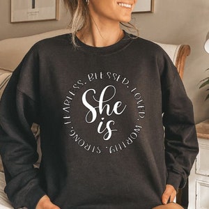May include: Black sweatshirt with a white circle graphic that says "She is" surrounded by the words "Worthy, Loved, Blessed, Fearless, Strong".