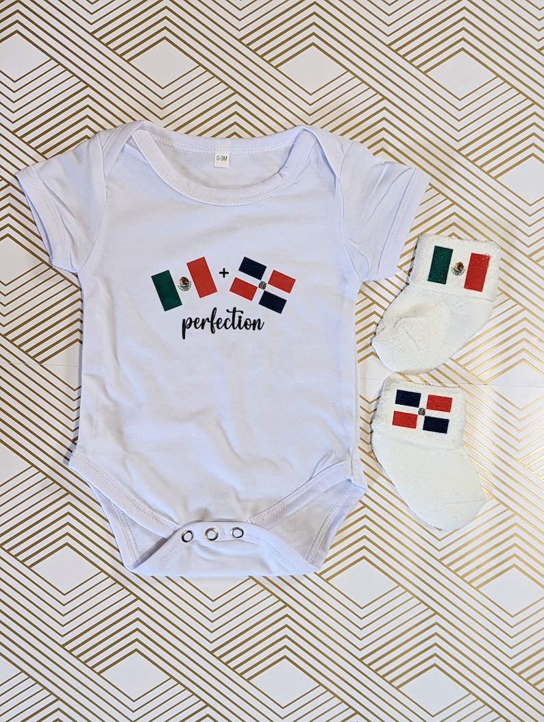 May include: White baby onesie with a graphic of two flags, a Mexican flag and a Dominican Republic flag, with the text " + perfection". The onesie is paired with a pair of white baby socks, one with a Mexican flag and the other with a Dominican Republic flag.