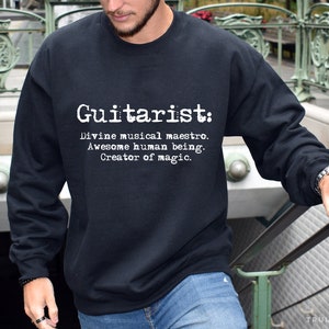 May include: A black sweatshirt with white text that reads "Guitarist: Divine musical maestro. Awesome human being. Creator of magic."