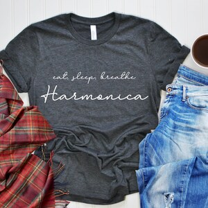 May include: A dark gray t-shirt with the text "eat, sleep, breathe harmonica" in white lettering.