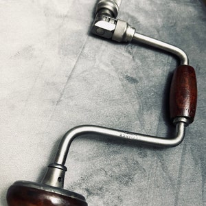 May include: A silver brace with a wooden handle and a metal crank. The brace is labeled "STEELANCE" and has a small hole in the metal crank.