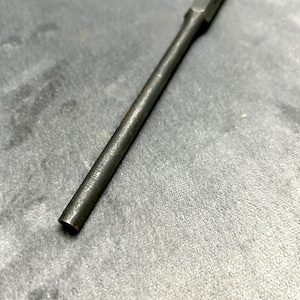 May include: A long, thin, metal rod with a squared end. The rod is silver in color and has a smooth, polished finish.