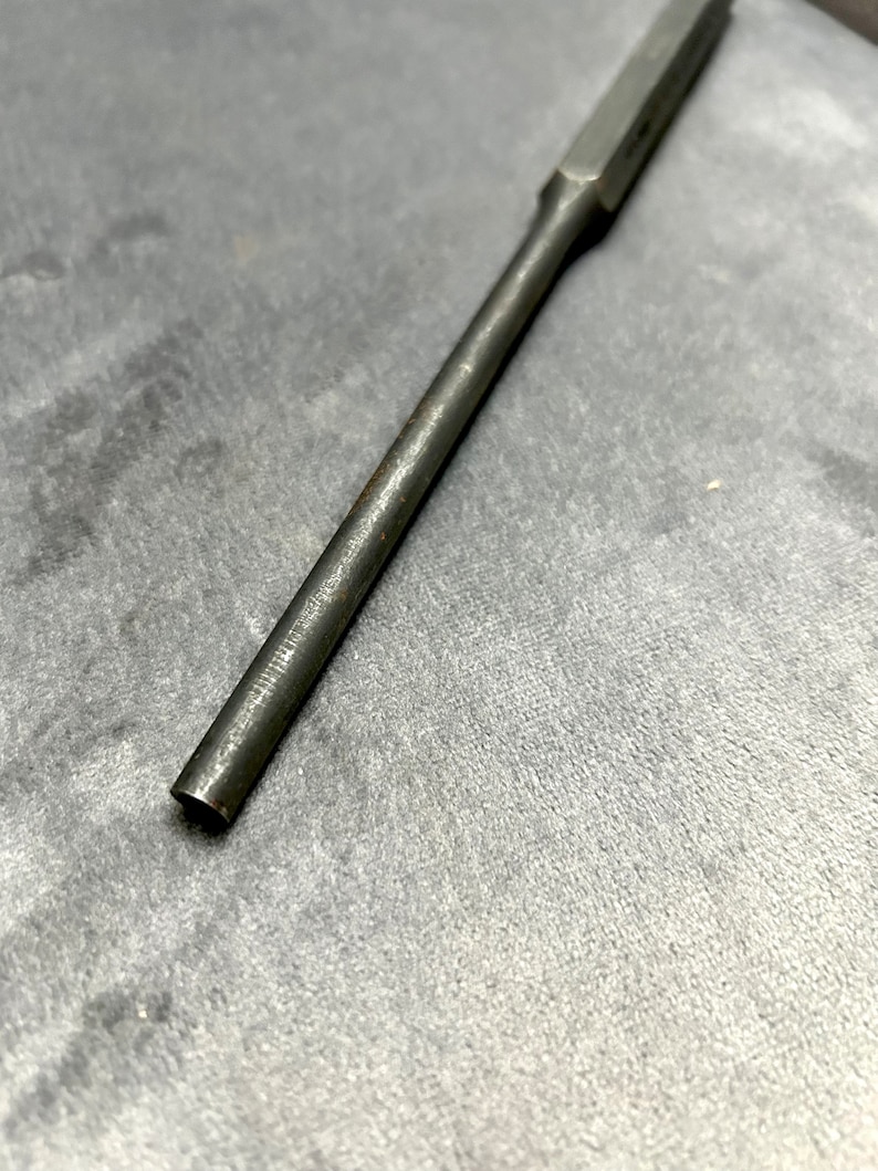 May include: A long, thin, metal rod with a squared end. The rod is silver in color and has a smooth, polished finish.