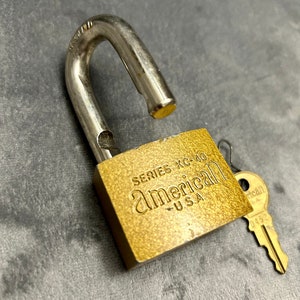 May include: A gold padlock with the text "SERIES KC-40 american - USA" on the front. The padlock is open and a brass key is lying next to it.