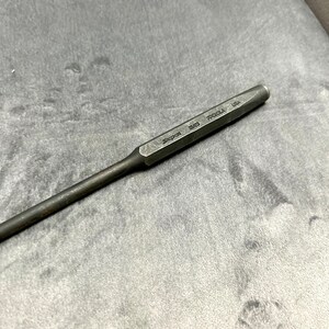 May include: A silver metal punch tool with the text "Snap-on 3/16" printed on the side. The tool is on a gray surface.
