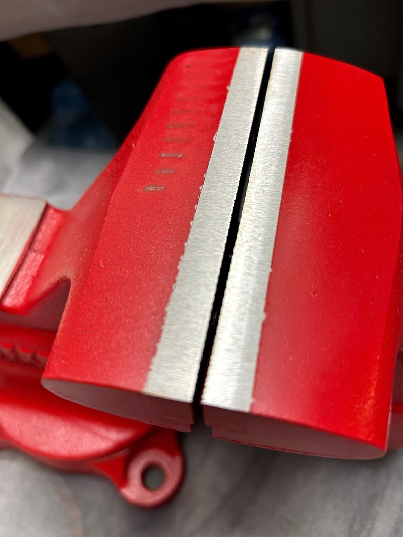 May include: A red metal vise with two silver jaws. The jaws are open and ready to clamp.