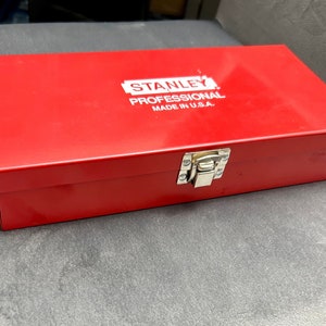 Puede incluir: Una caja de herramientas de metal roja con un cierre plateado. La caja tiene las palabras "STANLEY PROFESSIONAL MADE IN U.S.A." impresas en blanco en la tapa.