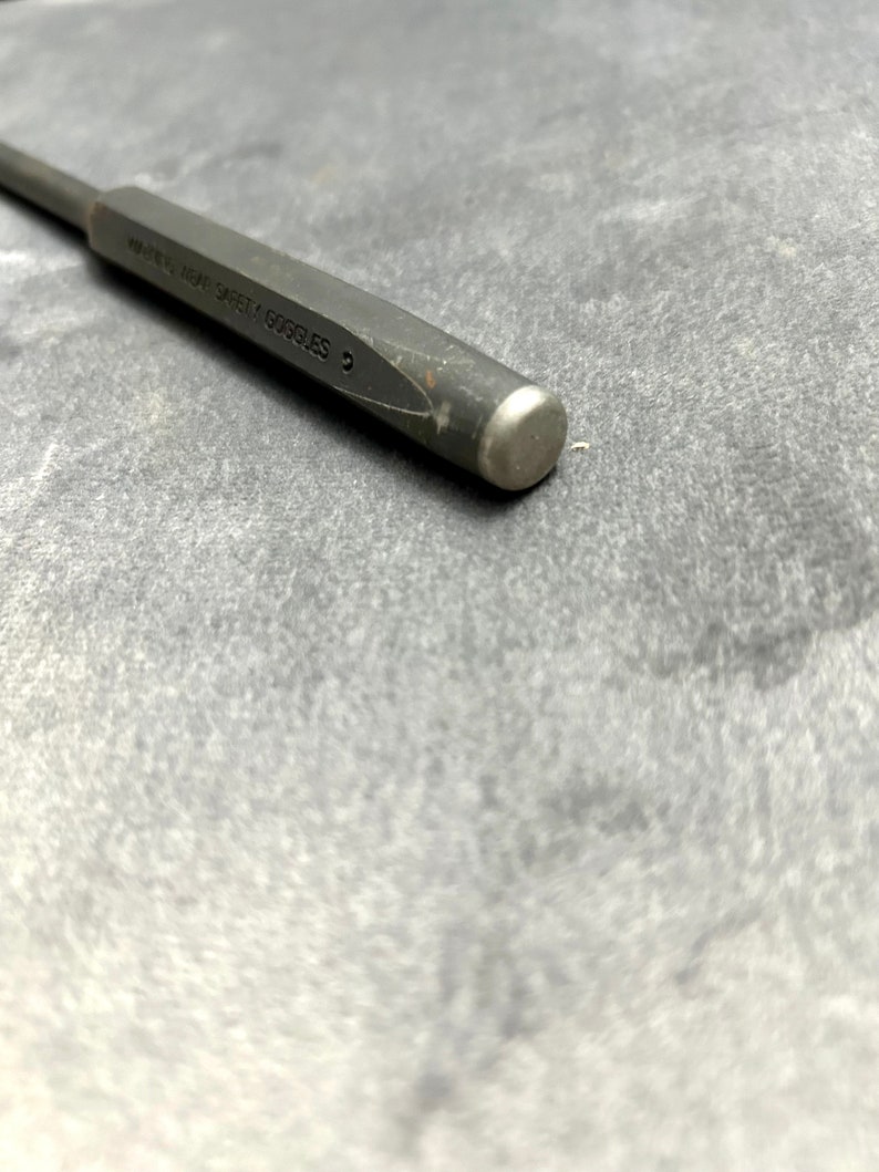 May include: A close-up of a gray metal punch tool with the text "WEAR HEAT SAFETY GOGGLES" engraved on the side.