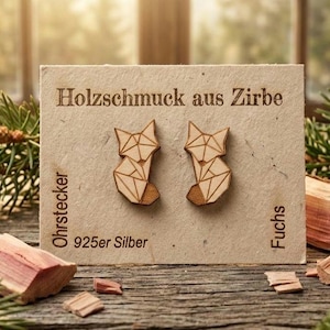 Könnte beinhalten: Geometrische Holzohrringe in Fuchform auf einer Karte mit deutschem Text. Die Ohrringe sind hellbraun. Auf der Karte steht auch "925er Silber". Der Hintergrund umfasst Holz, Grün und ein Fenster.