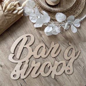 Peut inclure: Une pancarte en bois avec les mots "Bar & Crops" en écriture cursive. La pancarte est posée sur une surface en bois brun clair.