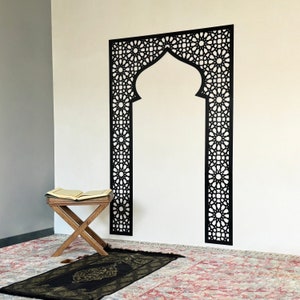 May include: A black decorative wall decal with an intricate geometric design, resembling an archway. A prayer rug and a small wooden stool with an open book are in the foreground.