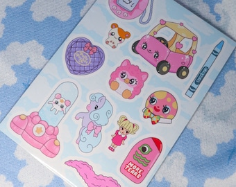 May include: A sheet of colorful stickers featuring various cute cartoon characters and objects. Includes a pink Tamagotchi, a heart-shaped Polly Pocket, a pink car, a crayon, and other whimsical designs. The background is a light blue with a cloud pattern.