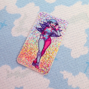 Puede incluir: Una pegatina brillante con un personaje pixelado con ropa azul y rosa, una cara blanca y una sonrisa roja. La pegatina está sobre un fondo azul claro.