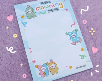 May include: A light blue notepad with the text "NO MORE clowning AROUND!" and illustrations of cartoon clowns. The notepad has a light blue border with decorative hearts, stars, and confetti. The notepad is from the Dipstick Store.