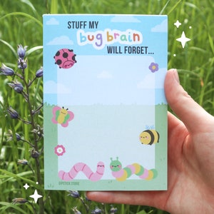 May include: A blue notepad with the text "Stuff my bug brain will forget..." in white and rainbow lettering. The notepad has a green border and features cartoon illustrations of a ladybug, butterfly, bee, and worm.