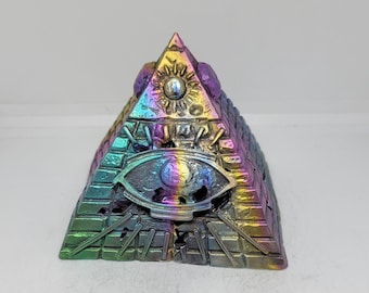 Op de afbeelding: Een veelkleurige piramide met een alziend oogontwerp. De piramide is gemaakt van metaal en heeft een regenboogkleurige, iriserende afwerking.
