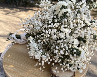 Pode incluir: Um buquê de flores brancas de gipsofila amarradas com barbante, descansando sobre uma superfície de madeira.